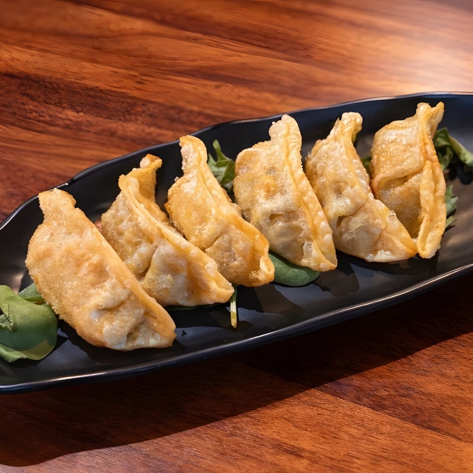 Six crispy fried gyoza dumplings, garnished with green leaves, on a black rectangular plate.