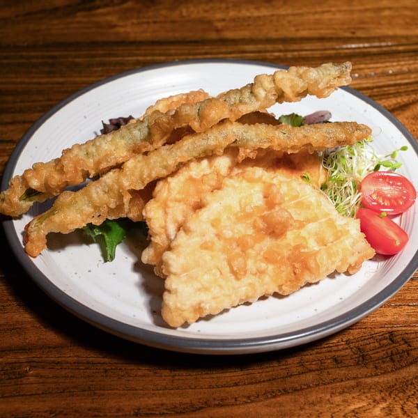Crispy tempura-fried green beans and flat vegetables, garnished with sprouts and cherry tomatoes on a white plate.