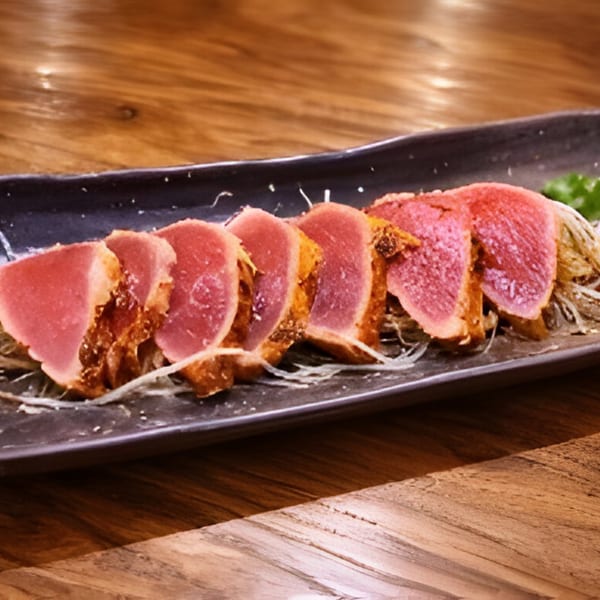 Seared tuna tataki slices with a pink center and golden-brown edges, served on a dark plate.
