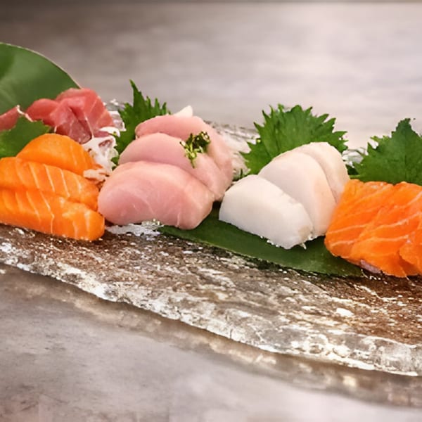 Assorted sashimi slices, including salmon, tuna, and white fish, garnished with green leaves on a stone plate.