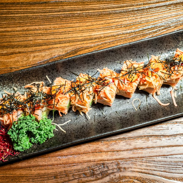 Kiwami Ramen Sushi's California roll topped with crab sticks, sauce, and nori, on a black plate.