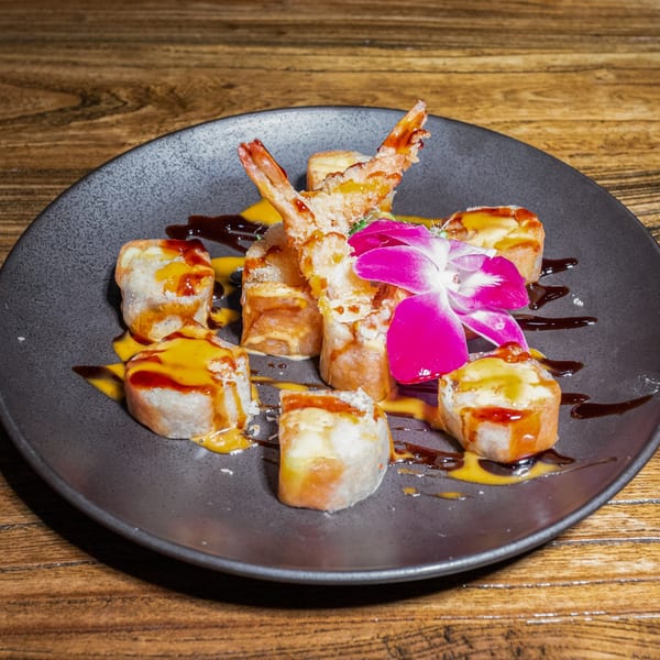 Kiwami Ramen Sushi's fried shrimp and sushi rolls with sauces and a pink orchid on a dark plate.