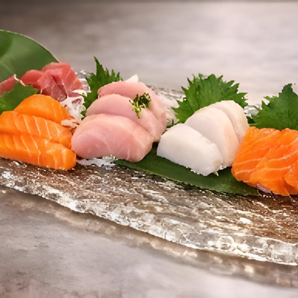 Assortment of fresh sashimi, including salmon, tuna, and white fish, garnished with green leaves.
