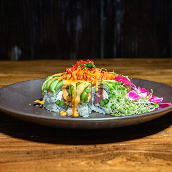Kiwami Ramen Sushi's vibrant sushi roll with avocado, sauces, roe, and microgreens on a dark plate.