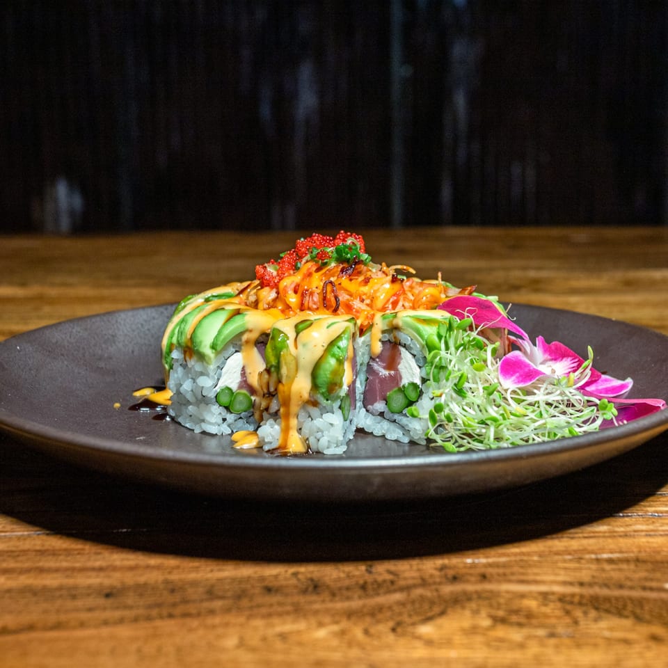 Kiwami Ramen Sushi's vibrant sushi roll with avocado, sauces, roe, and microgreens on a dark plate.